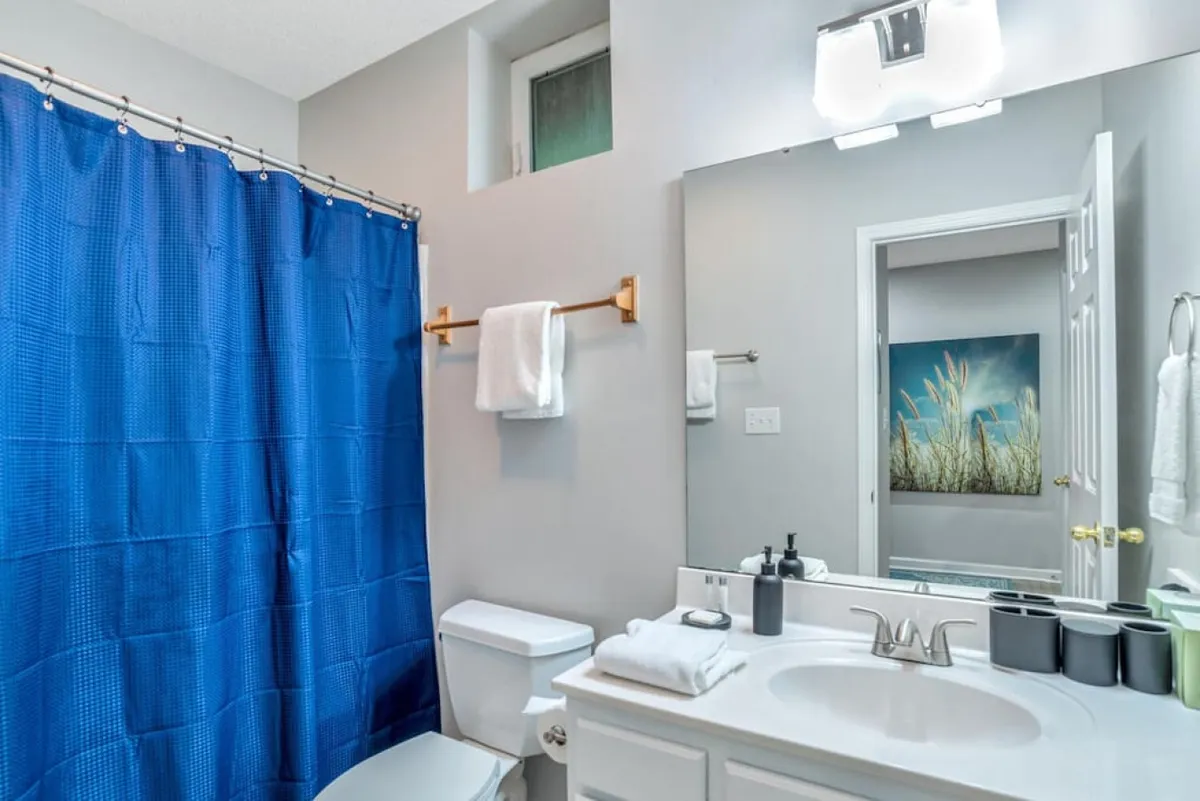 A modern bathroom featuring a blue shower curtain, a sleek vanity with a sink, and neatly arranged towels. The overall vibe is refreshing and spa-like, emphasizing comfort and relaxation.