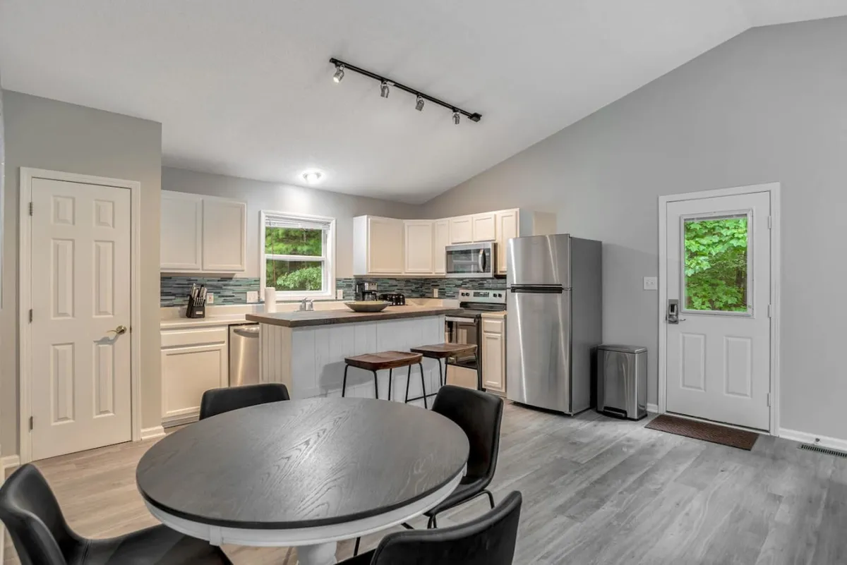 The image captures a kitchen island, a dining table, and large windows that flood the space with light. The setup is ideal for family meals, social gatherings, and casual conversation. The modern furnishings and airy feel create a welcoming environment.