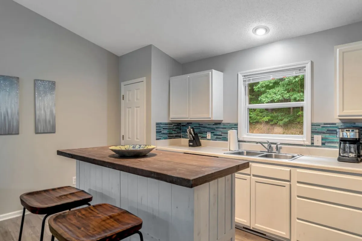 A welcoming kitchen scene with a prominent island, modern sink, a large window, and tasteful decor including a decorative bowl. The setting feels ready for both cooking and entertaining, with natural light enhancing its appeal. The window view connects guests to the outdoors, while the island serves as a natural gathering spot.