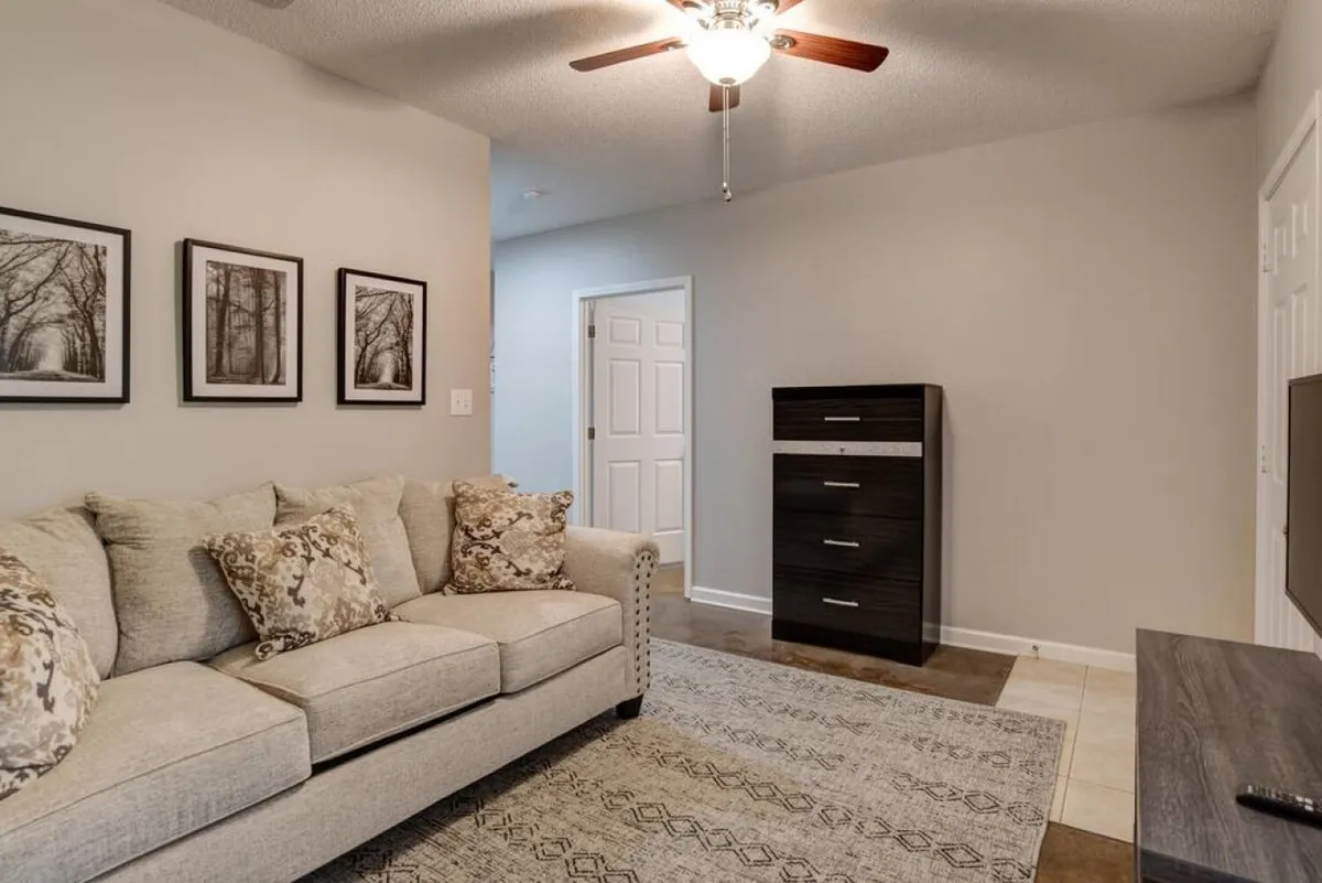 A welcoming living room with a cozy sofa decorated with colorful throw pillows, complemented by modern wall art and a dresser. The space feels airy and inviting, perfect for group gatherings or unwinding after an evening out.