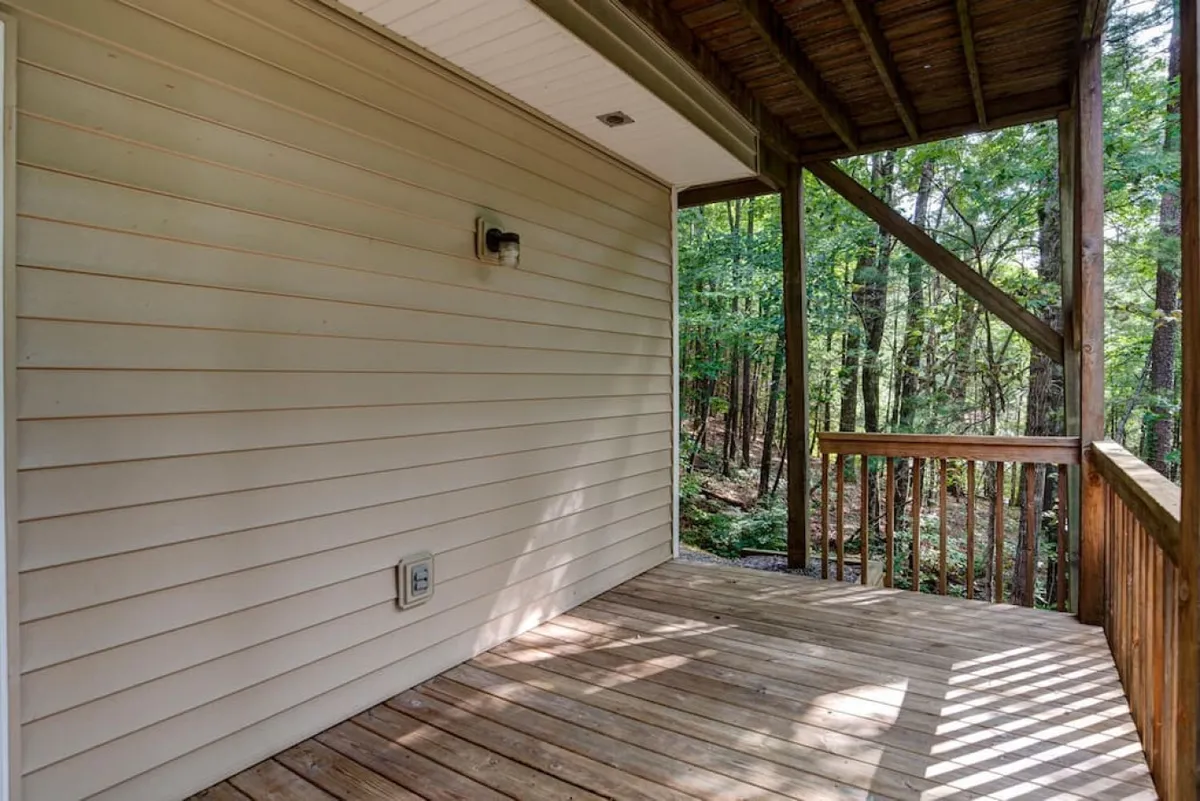 A peaceful wooden deck is set amidst tall trees, with the house siding visible in the background. The natural setting evokes the serenity of outdoor living, perfect for relaxing with pets after a day of adventure. The tranquility and privacy of the space suggest a seamless connection between indoor comfort and outdoor enjoyment.